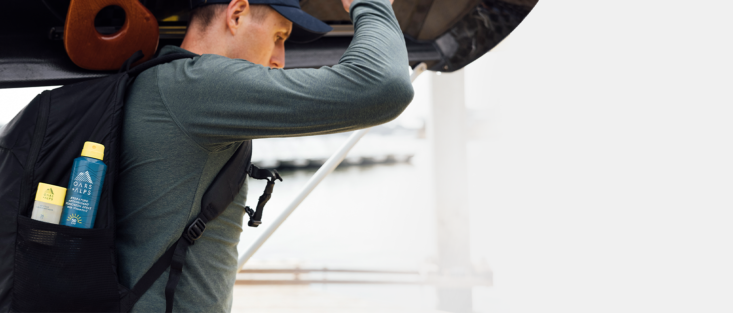 man carrying boat overhead with Oars and Alps products in his backpack